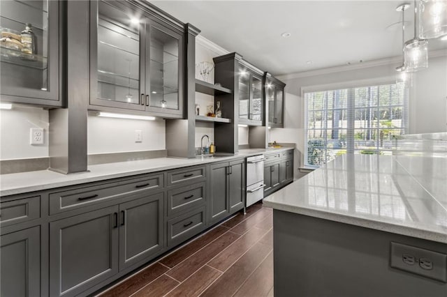 kitchen with a sink, gray cabinets, ornamental molding, dark wood-style flooring, and glass insert cabinets