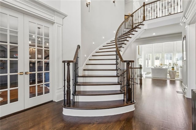 stairs with french doors, wood finished floors, and a towering ceiling