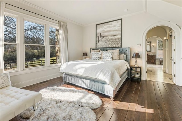 bedroom with baseboards, lofted ceiling, ornamental molding, hardwood / wood-style flooring, and arched walkways