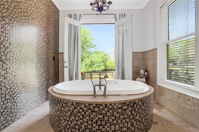 bathroom featuring a wealth of natural light, a notable chandelier, tile walls, and a freestanding tub