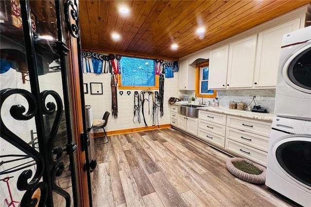 laundry room with light wood-type flooring, laundry area, wooden ceiling, stacked washer / drying machine, and a sink