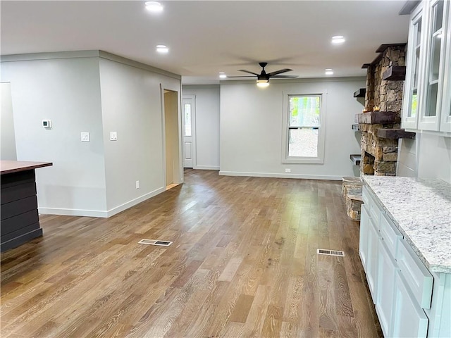 unfurnished living room with ceiling fan, a stone fireplace, and light wood-type flooring