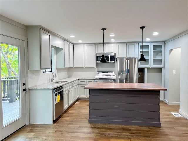 kitchen featuring sink, appliances with stainless steel finishes, a center island, light stone counters, and decorative light fixtures