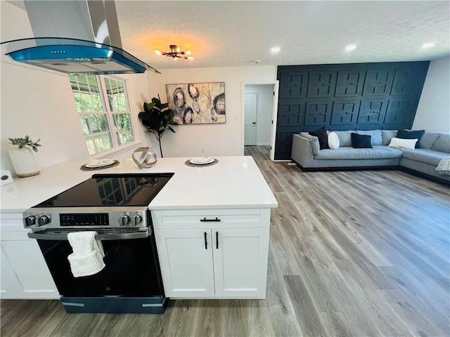 kitchen with stainless steel range with electric stovetop, island range hood, light wood-type flooring, and white cabinets