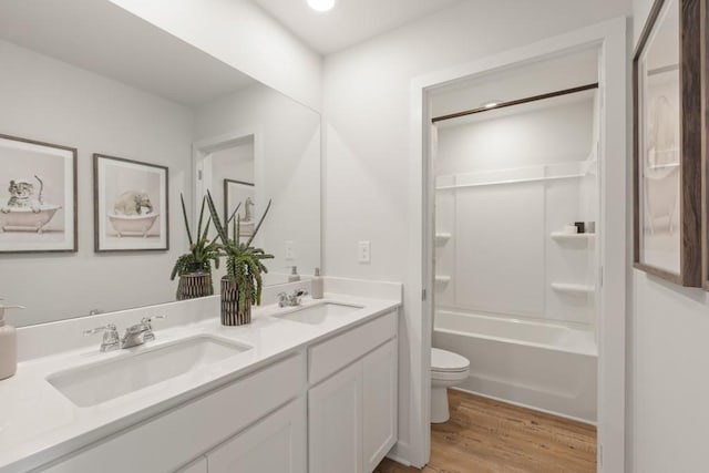 full bath with double vanity, wood finished floors, a sink, and toilet