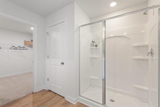 full bath with a shower stall, baseboards, a walk in closet, and wood finished floors