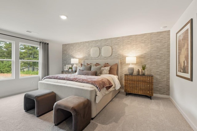 carpeted bedroom with an accent wall, visible vents, and baseboards