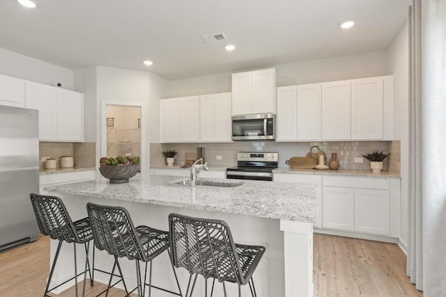 kitchen with light wood finished floors, visible vents, white cabinets, stainless steel appliances, and a sink