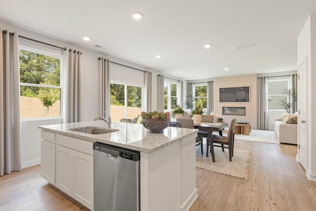 kitchen featuring an island with sink, open floor plan, light wood-type flooring, stainless steel dishwasher, and a sink