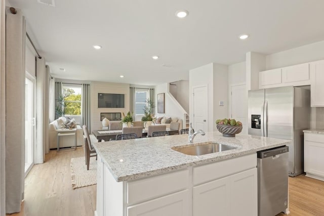 kitchen with appliances with stainless steel finishes, an island with sink, a sink, and white cabinetry