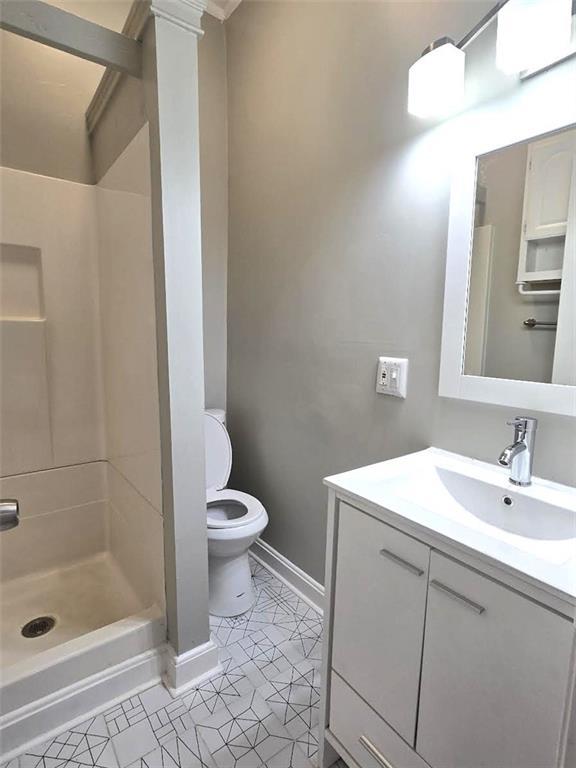 bathroom featuring tile patterned flooring, baseboards, toilet, a stall shower, and vanity