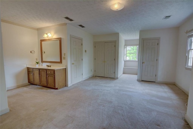 unfurnished bedroom with light carpet, a textured ceiling, baseboards, and ensuite bathroom