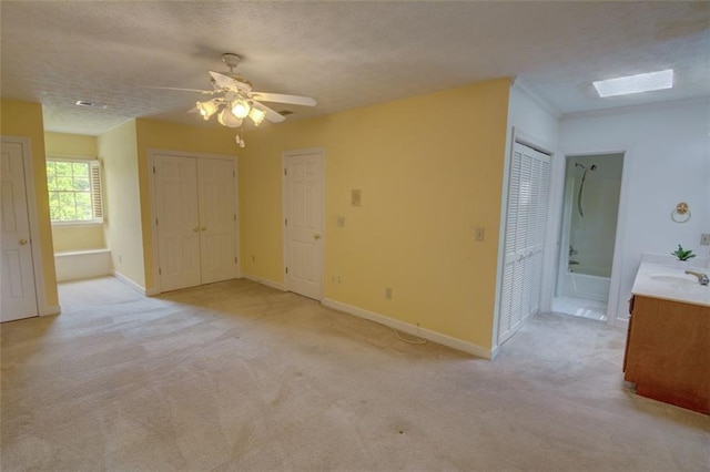 spare room featuring a sink, light carpet, a ceiling fan, a skylight, and a textured ceiling