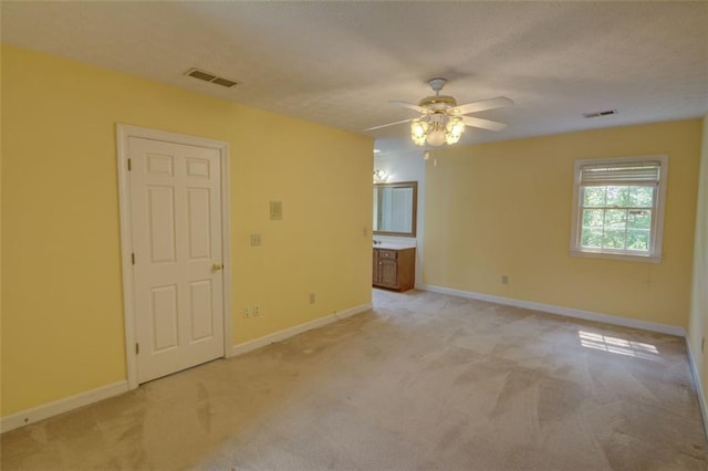 spare room featuring light carpet, ceiling fan, baseboards, and a textured ceiling