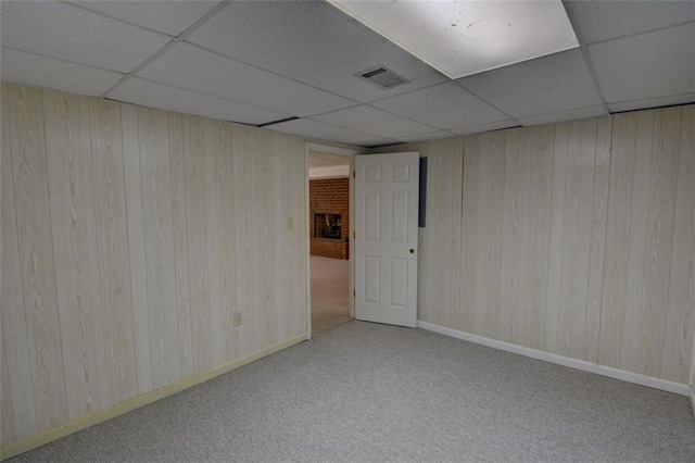 carpeted empty room with a drop ceiling, wood walls, and baseboards