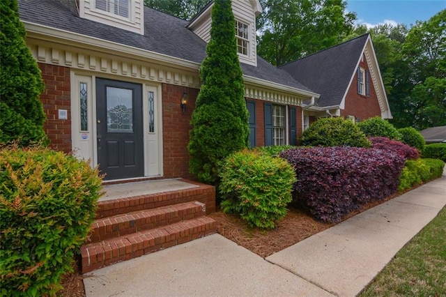 doorway to property featuring brick siding and a shingled roof