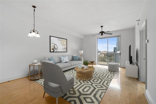 living room featuring ceiling fan with notable chandelier and light wood-type flooring