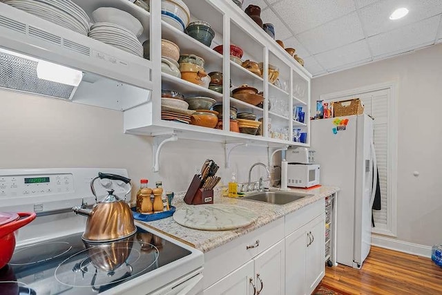 kitchen with ventilation hood, white appliances, white cabinets, light stone counters, and sink