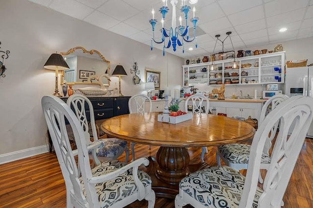 dining space with an inviting chandelier, wood-type flooring, a drop ceiling, and sink