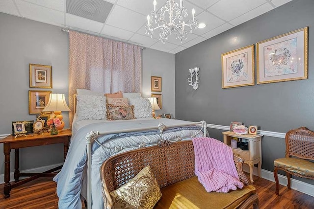 bedroom with a drop ceiling, hardwood / wood-style floors, and an inviting chandelier