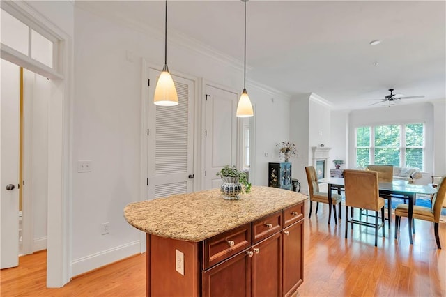 kitchen with hanging light fixtures, light stone counters, a kitchen island, light hardwood / wood-style floors, and ceiling fan