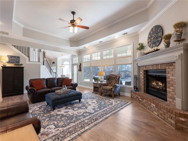 living room featuring ceiling fan, crown molding, wood-type flooring, and a brick fireplace