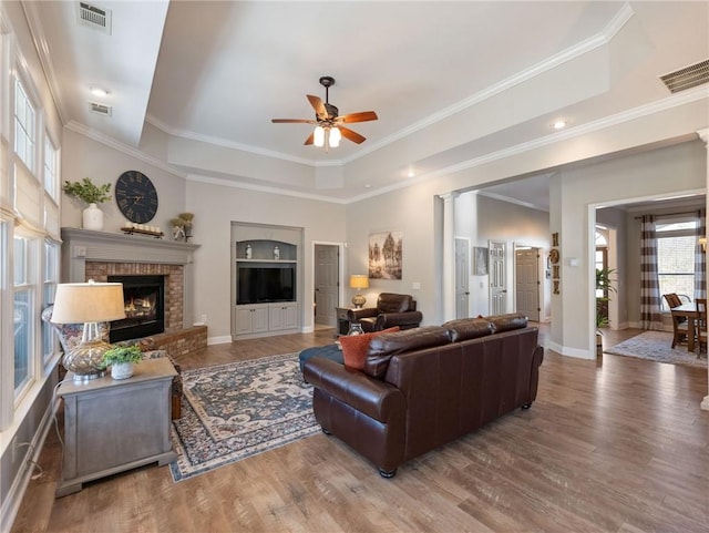 living room featuring ceiling fan, a fireplace, wood-type flooring, and a tray ceiling