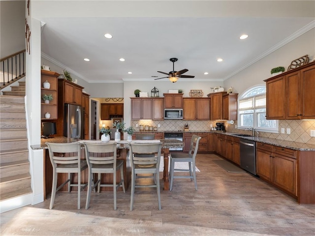 kitchen with a breakfast bar area, appliances with stainless steel finishes, light wood-type flooring, ornamental molding, and a center island