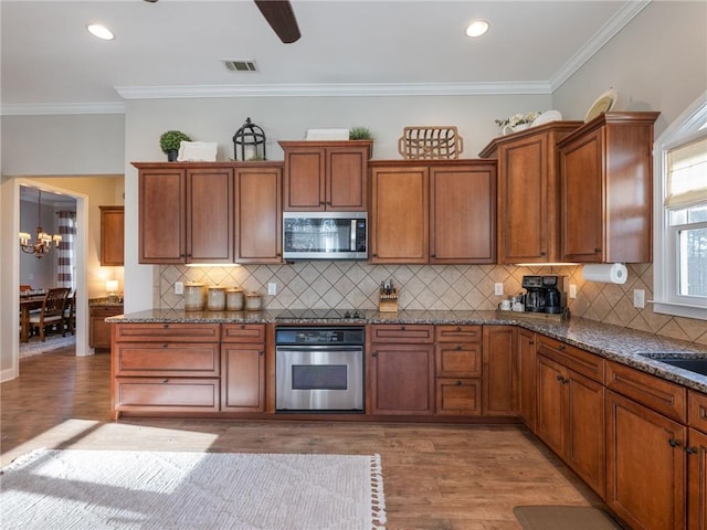 kitchen with an inviting chandelier, stainless steel appliances, ornamental molding, and wood-type flooring