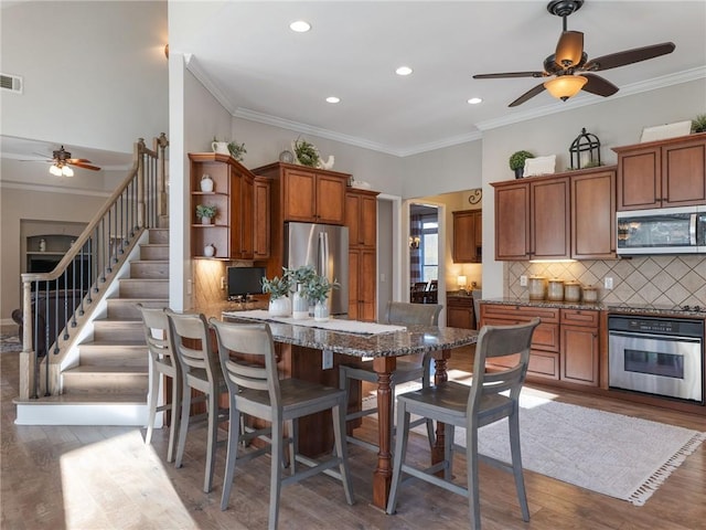 kitchen featuring a kitchen bar, hardwood / wood-style flooring, kitchen peninsula, appliances with stainless steel finishes, and decorative backsplash