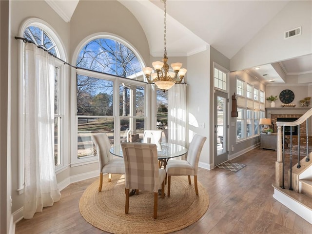 dining area featuring a fireplace, a notable chandelier, ornamental molding, and hardwood / wood-style floors