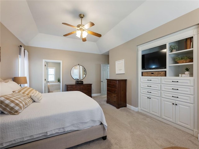 bedroom with connected bathroom, light carpet, vaulted ceiling, ceiling fan, and a tray ceiling