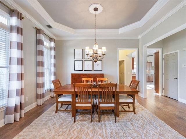 dining space featuring crown molding, hardwood / wood-style floors, a tray ceiling, and a notable chandelier