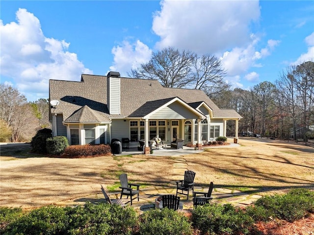 back of property with a fire pit, a lawn, and a patio