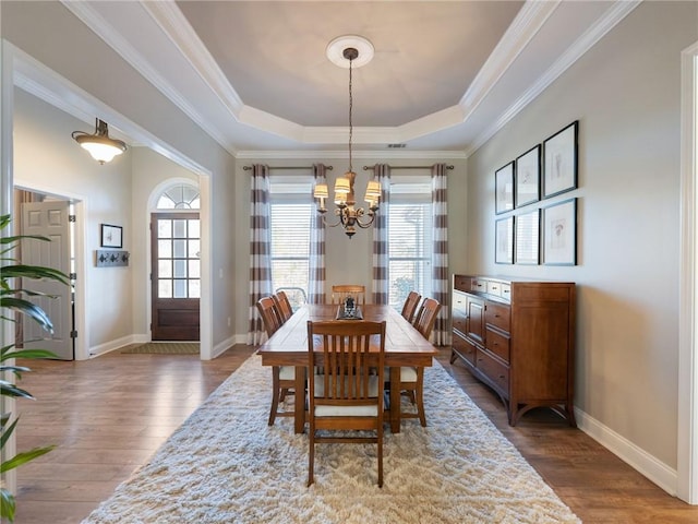 dining space featuring crown molding, an inviting chandelier, a tray ceiling, and hardwood / wood-style floors