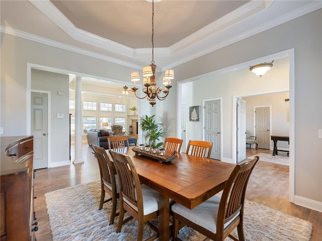 dining room with an inviting chandelier, decorative columns, a raised ceiling, ornamental molding, and light hardwood / wood-style flooring