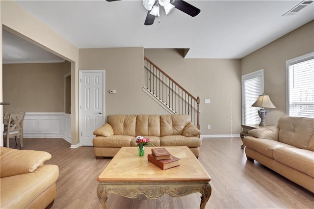 living area with visible vents, a wainscoted wall, a ceiling fan, stairway, and light wood-style floors