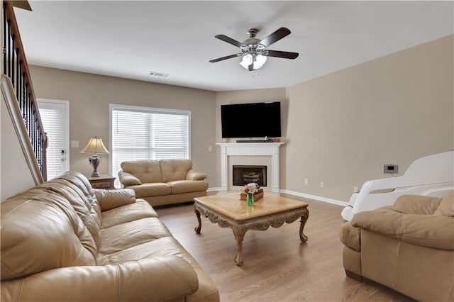 living area with visible vents, a ceiling fan, a fireplace, light wood finished floors, and baseboards