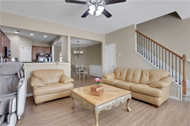 living room with light wood-type flooring, ceiling fan with notable chandelier, recessed lighting, wainscoting, and stairs