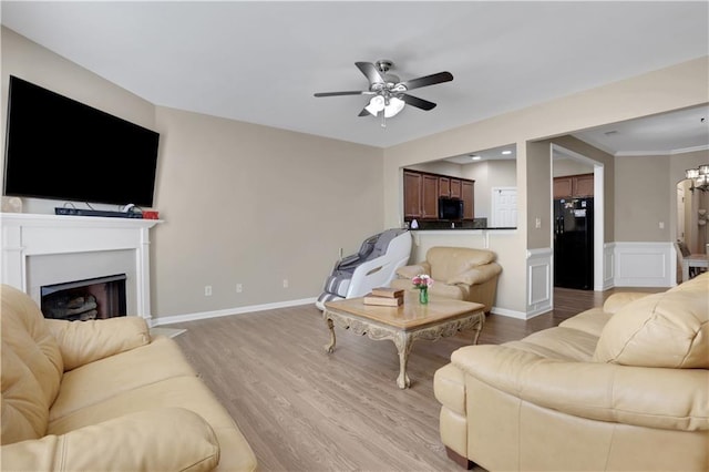 living area with a ceiling fan, baseboards, a fireplace, wainscoting, and light wood-type flooring