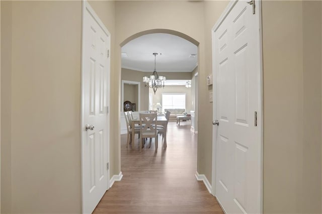 corridor featuring a notable chandelier, wood finished floors, arched walkways, and baseboards