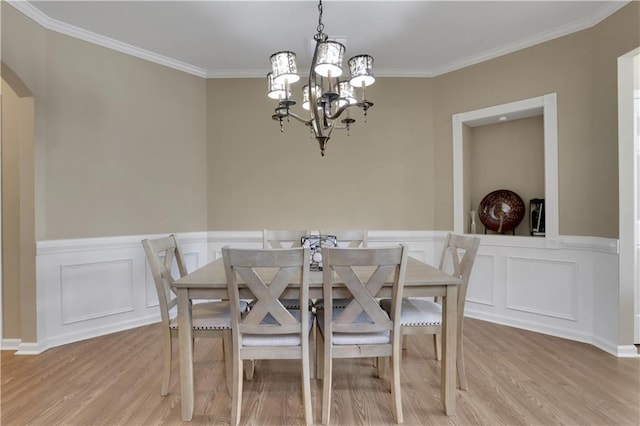 dining space featuring arched walkways, light wood-style flooring, crown molding, and an inviting chandelier