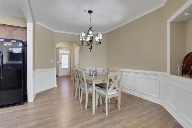 dining area featuring light wood finished floors, a notable chandelier, ornamental molding, arched walkways, and a decorative wall