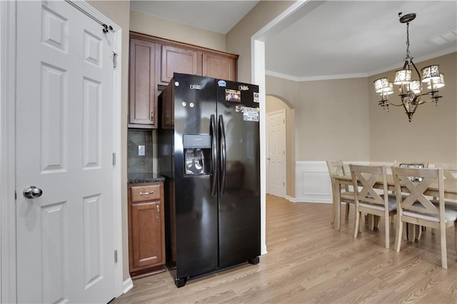 kitchen with crown molding, light wood-style flooring, black fridge with ice dispenser, and arched walkways