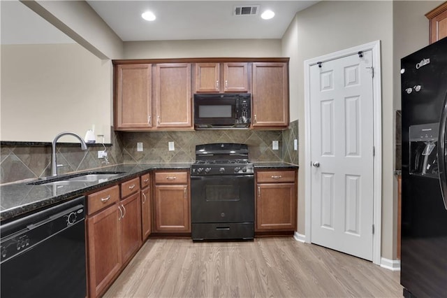 kitchen with tasteful backsplash, visible vents, light wood-type flooring, black appliances, and a sink