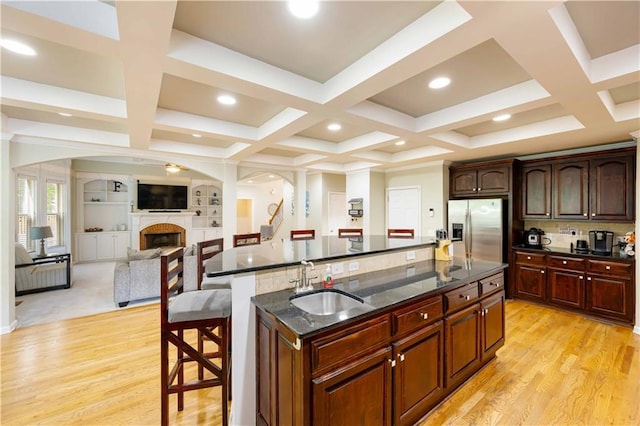 kitchen with a sink, stainless steel fridge, a breakfast bar area, a center island with sink, and a fireplace
