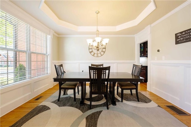 dining area with a chandelier, wood finished floors, a raised ceiling, ornamental molding, and wainscoting