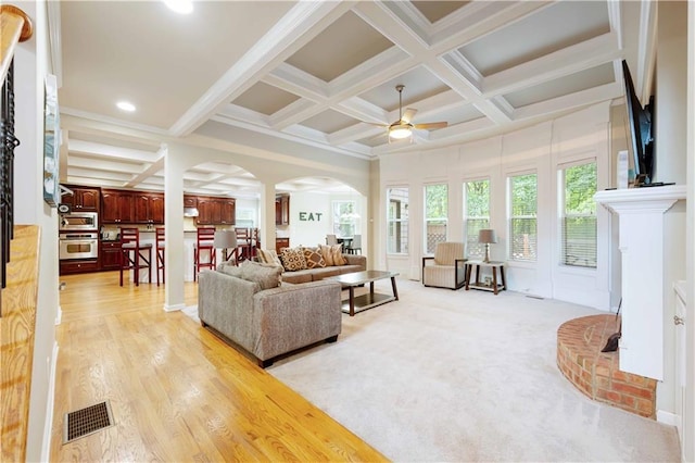 living area featuring arched walkways, coffered ceiling, ceiling fan, beam ceiling, and light wood-style flooring