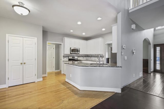 kitchen featuring sink, light wood-type flooring, dark stone counters, stainless steel appliances, and white cabinets