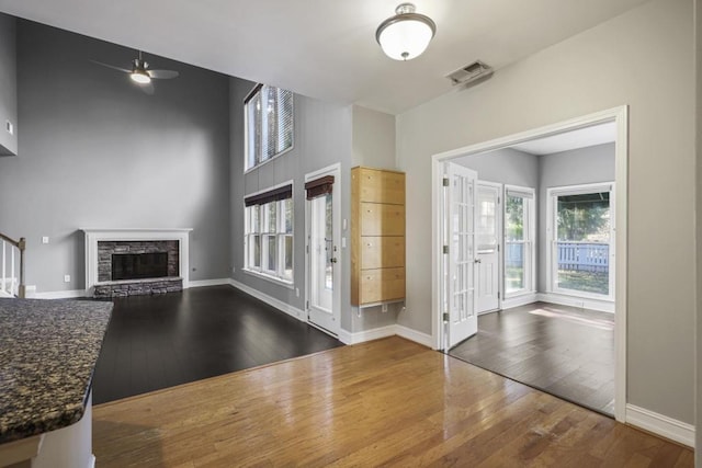 foyer entrance featuring hardwood / wood-style flooring, ceiling fan, a healthy amount of sunlight, and a stone fireplace